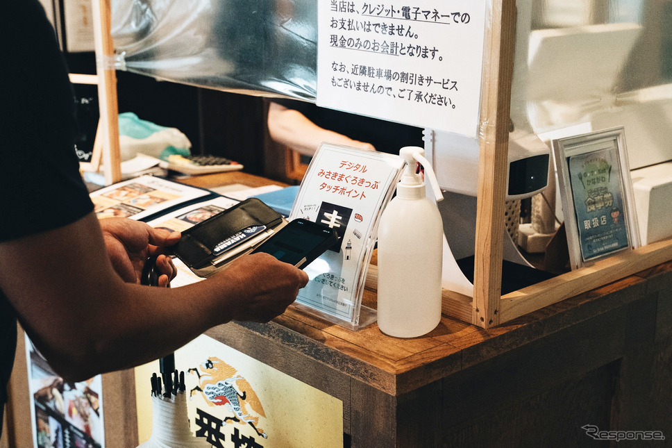 三崎港魚市場食堂で「まんぷく券」をかざす《写真撮影 坂本貴史》