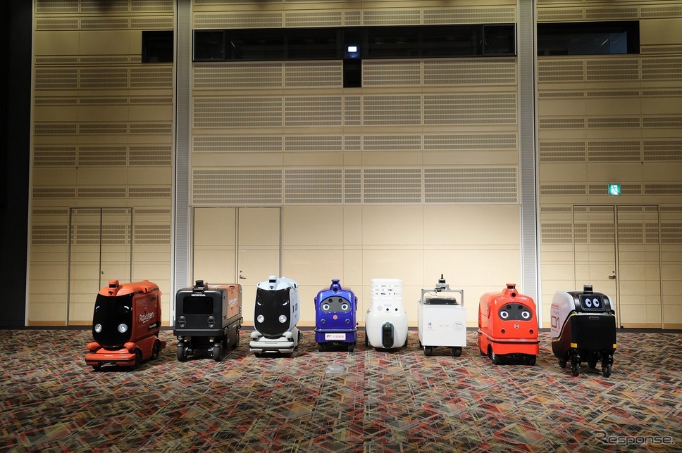 ロボットデリバリー協会各社の自動配送ロボット：向かって右から川崎重工業、ZMP、TIS、ティアフォー、日本郵便、パナソニック、本田技研工業、楽天グループ《写真提供 パナソニック》